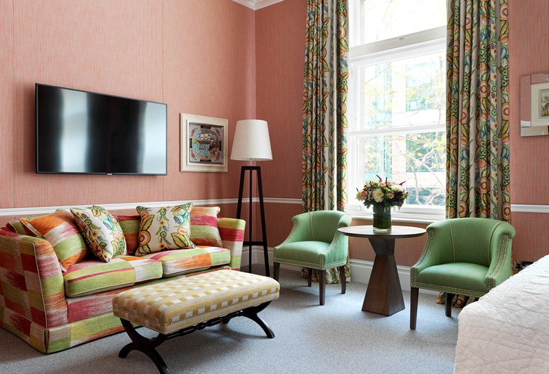 Pattern wallpaper with two arm chairs and a small table. The headboard reflects on the mirror panel behind the chairs