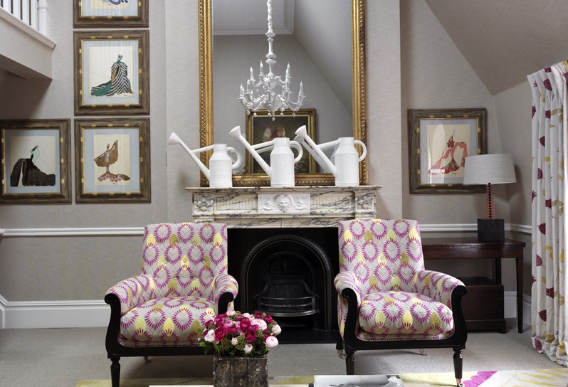 Sitting room of the Loft Suite at Covent Garden Hotel showing two arm chairs and a fireplace with a mirror on top, you can also see a small corner of the mezzanine on the right side