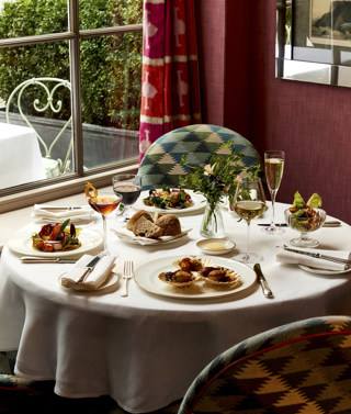 A table in front of a window at Brumus laid with four appetisers accompanied by glasses of wine and cocktails