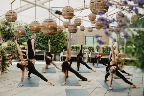 An image of Equinox instructors doing a yoga class to promote the series of classes hosted by Equinox on Ham Yard Hotels Roof Terrace.