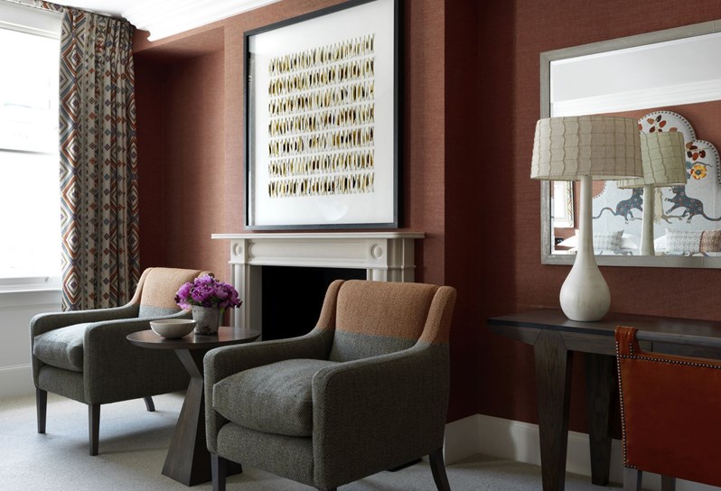 Suite sitting area with two chairs, a fireplace with a beautifully framed piece of artwork and desk with mirror to the right.