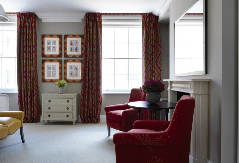 Two deep red chairs in front of a fireplace in a Suffolk suite. In the background are large windows with four pieces of art in between them