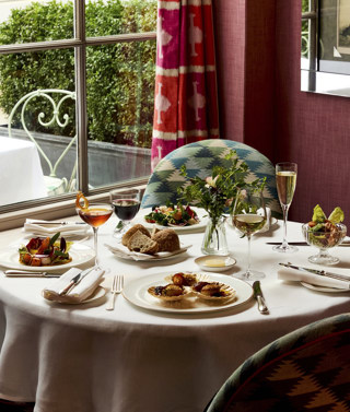 A table in front of a window at Brumus laid with four appetisers accompanied by glasses of wine and cocktails