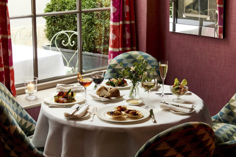 A table in front of a window at Brumus laid with four appetisers accompanied by glasses of wine and cocktails