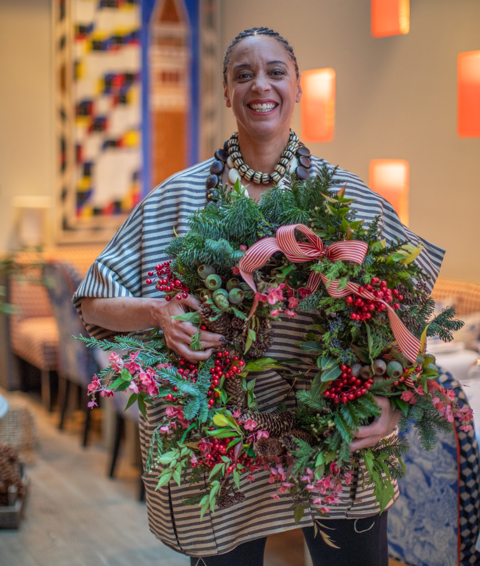 A portrait of florist Tawana Schlegel holding a wreath in the Orangery at Warren Street Hotel
