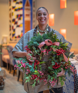 A portrait of florist Tawana Schlegel holding a wreath in the Orangery at Warren Street Hotel