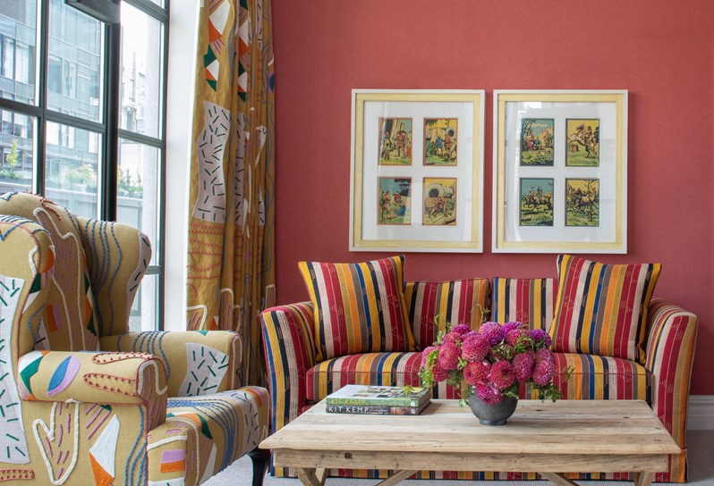 A large, whimsical living room with inviting lounge furniture and bold colors looking over a terrace, with flowers on the coffee table table