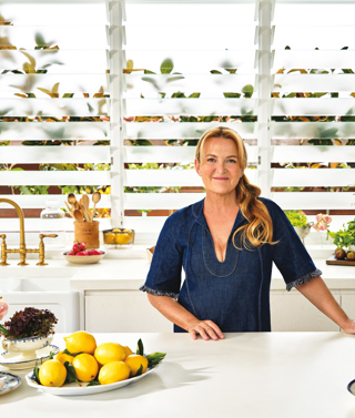Chef Donna Hay in a white kitchen. She is standing against a worktop, which has plates of ingredients on