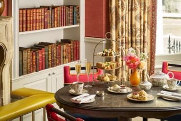 Afternoon tea displayed on a table in the library at the Knightsbridge Hotel. The fine bone china is Mythical Creatures by Kit Kemp for Wedgwood along side a 3 tier cake stand, sandwiches and scones.