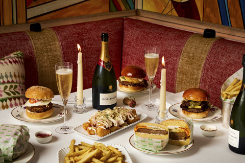 A landscape image of multiple dishes from the New Years Day, Bollinger and Burgers Menu at Oscar, Charlotte Street Hotel. On the table, you can see multiple burgers and a bottle and glasses filled with Bollinger Champagne. 