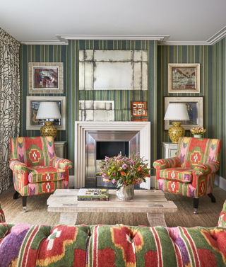 Living room shot of Residence 09, a Luxury Two Bedroom Residence at Ham Yard Hotel. A portrait mage from the back of the sofa, in a bold green and orange print, looking towards armchairs the face the viewer in the same print. A coffee table topped with books and flowers sit in the centre.