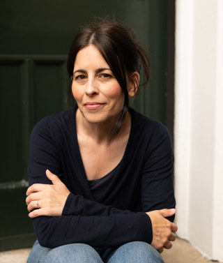 A headshot of author Florence Knapp, she sits on a step outside a front door