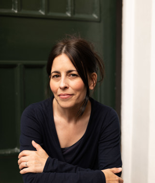 A headshot of author Florence Knapp, she sits on a step outside a front door