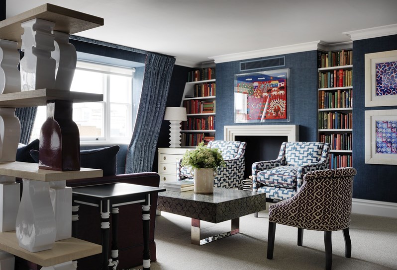 The Penthouse Suite lounge area facing a fireplace with bookshelves either side. Chairs face a coffee table in front and a window to the left streams light in.