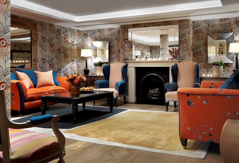 The Duncan Grant Room setup for a reception with sofas lining the walls. The room is decorated with a beautiful floral wallpaper and there is a large mirror hanging above a fireplace at the back of the room.