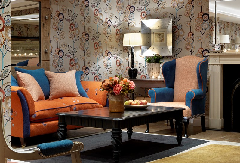 The Duncan Grant Room setup for an informal meeting with sofas and a coffee table. The room is decorated with a beautiful floral wallpaper and there is a large mirror hanging above a fireplace at the back of the room.