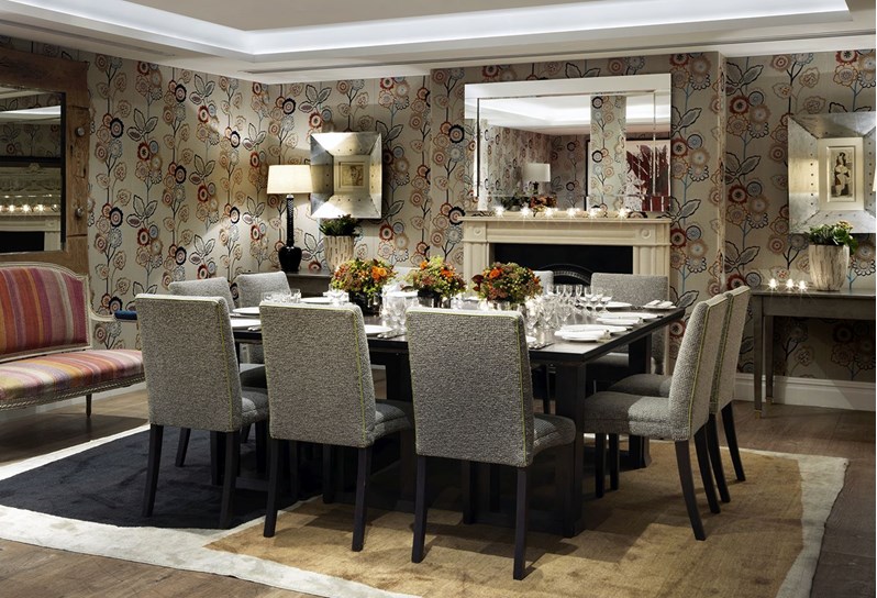 The Duncan Grant Room setup for a dinner on one table. The walls are decorated with a beautiful floral wallpaper and there is a large mirror hanging above a fireplace at the back of the room.