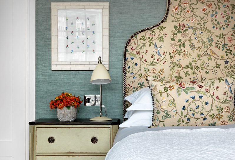 A close up detail image of a headboard in a neutral color with multicolored floral stitching