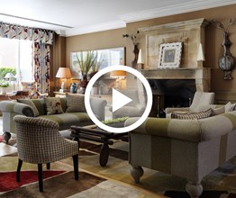 The drawing room at Charlotte Street Hotel with two striped green grey sofas around a handsome fireplace. Overlaid on the image is a play button icon.