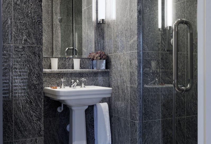 A granite bathroom containing a separate walk in shower, a basins, and a mirror.