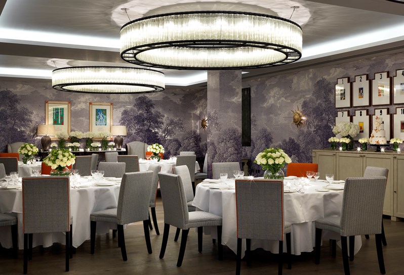 The Windmill room at HYH. A grey graphic wallpaper with a forest mural.  Several round tables are set up for a formal dinner.