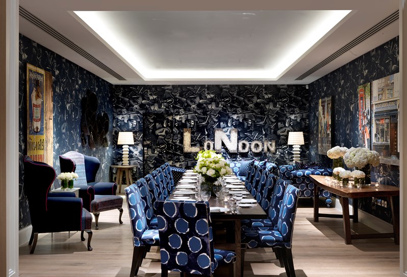 The Archer Room with Blue graphic wallpaper. Through the centre of the room is a banquette table with bright blue chairs.