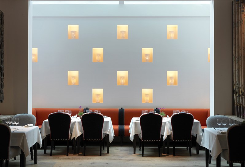 Illuminated porcelain pots by Martha Freud etched with earthy motives as an art installation on a wall behind beautifully set dining tables in Ham Yard Restaurant.