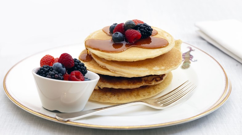 Close up image of a stack of American style pancakes garnished with mixed berries and maple syrup.