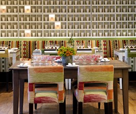 Beautifully set dining tables in The Potting Shed Restaurant in booths and at private tables, looking toward an art installation of illuminated porcelain pots by Martha Freud scattered on a wall.