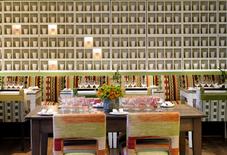 Beautifully set dining tables in The Potting Shed Restaurant in booths and at private tables, looking toward an art installation of illuminated porcelain pots by Martha Freud scattered on a wall.