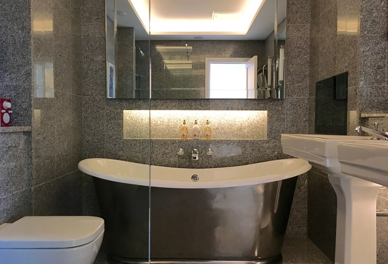 A grey marble bathroom with a gorgeous deep soaking tub straight ahead. On the right are double basins and on the left a standing shower.
