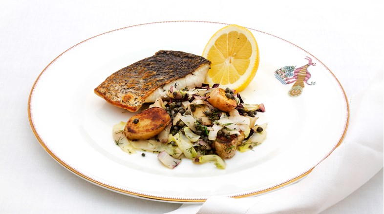 A close up image of a stone bass dish with sauteed vegetables and a half a lemon
