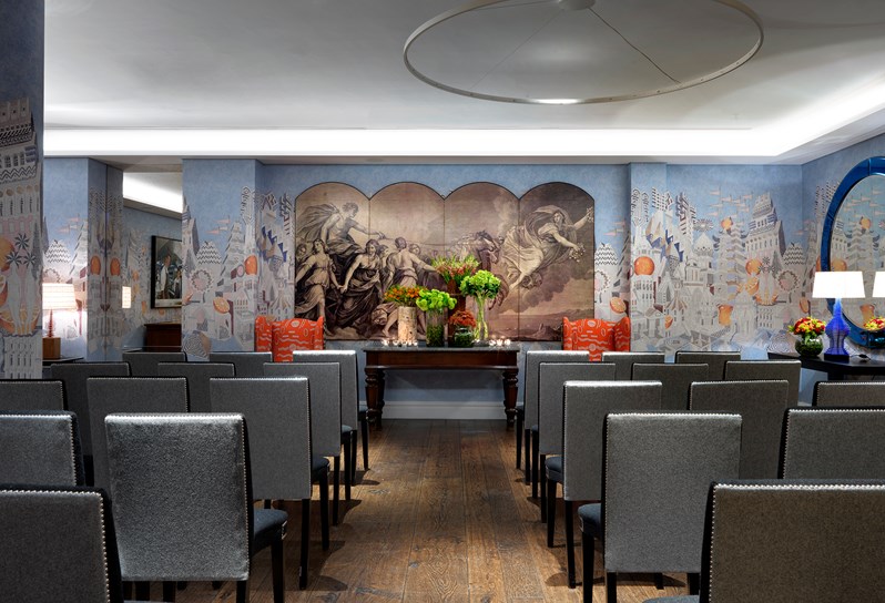 The Indigo Room is a private event space with light blue walls featuring an artistic pattern. It is set up with grey and blue chairs, theater style