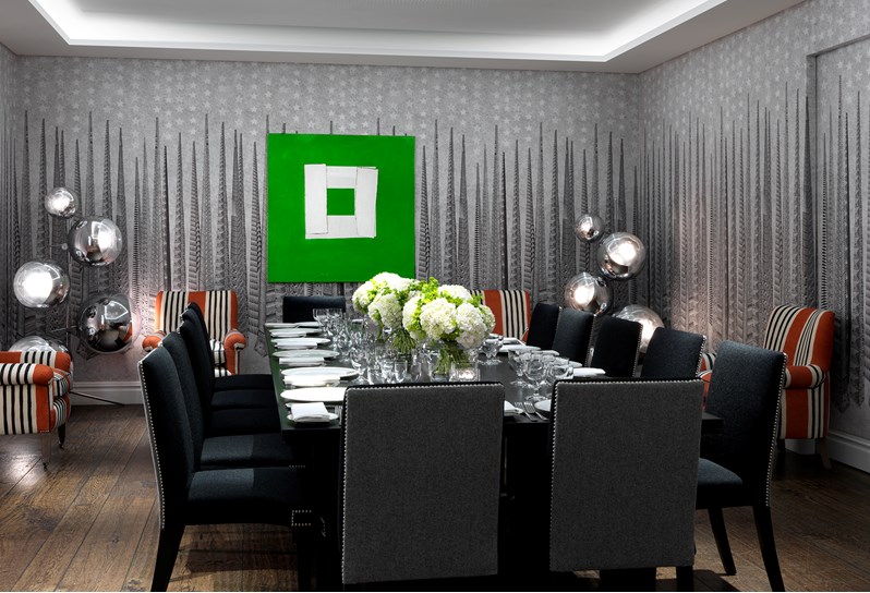 The Sandra Blow room at Soho Hotel. A grey graphic wallpaper and a black and white graphic carpet on the floor. There are four orange striped chairs, one large table set up board room style with black and grey chairs around it