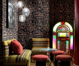 Soho Hotel Crimson Bar with a black patterned wallpaper, yellow stripe sofas and a bright neon Jukebox.