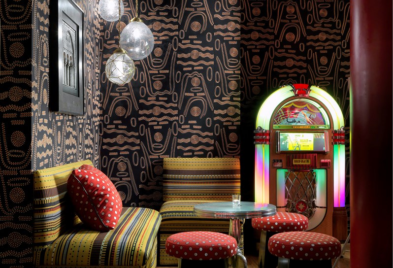 Soho Hotel Crimson Bar with a black patterned wallpaper, yellow stripe sofas and a bright neon Jukebox.