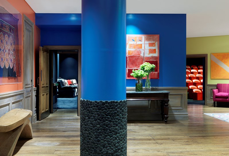 The lobby area of the private event floor at The Soho Hotel. Walls are cobalt blue. There is colorful artwork on the walls and oak wood floors. The image looks into the two private screening rooms.