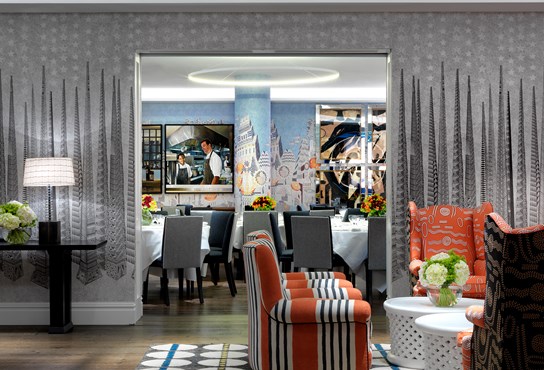 The Soho Hotel private event rooms. Sandra Blow Room with four orange arm chairs looks into the Indigo Room which is set for a private dinner on round tables with white linens. The Indigo Room is light blue in color