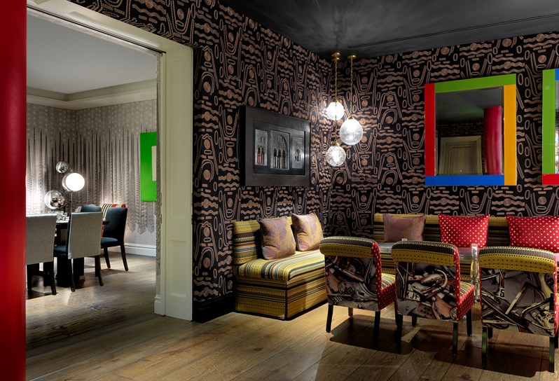 The Soho Hotel, Crimson Bar private event room. Dark fabric walls with a light pattern. Along one wall is low seating with two brightly colored mirrors above seating