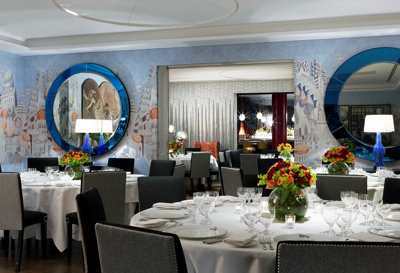 The Soho Hotel, Indigo private event room. The walls are light blue with an artistic print. Round tables are set up with white linens and chairs around them for a private dinner