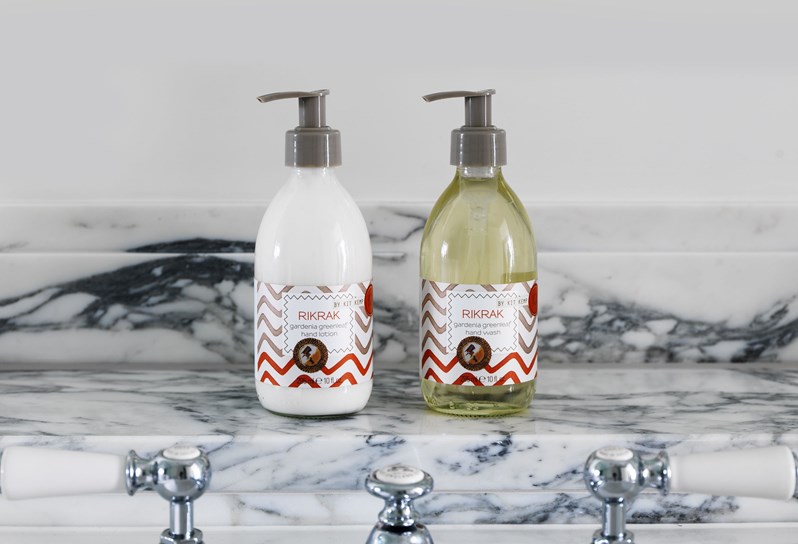 A bottle of Kit Kemp's signature Rik Rak hand lotion and a Rik Rak bottle of soap on a white marble shelf.