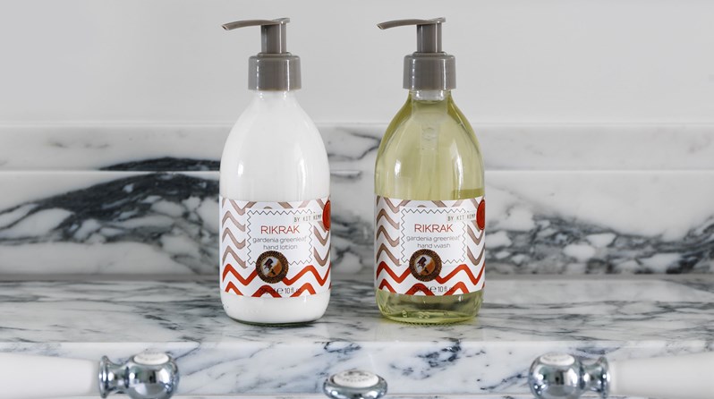 A bottle of Kit Kemp's signature Rik Rak hand lotion and a Rik Rak bottle of soap on a white marble shelf.