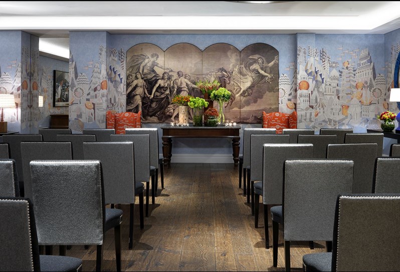 The Indigo Room at Soho Hotel set for intimate  wedding ceremony with rows of custom made grey and black cloth chairs facing forward. Colorful floral arrangements vary in size and candlelit votives set on display at the altar.