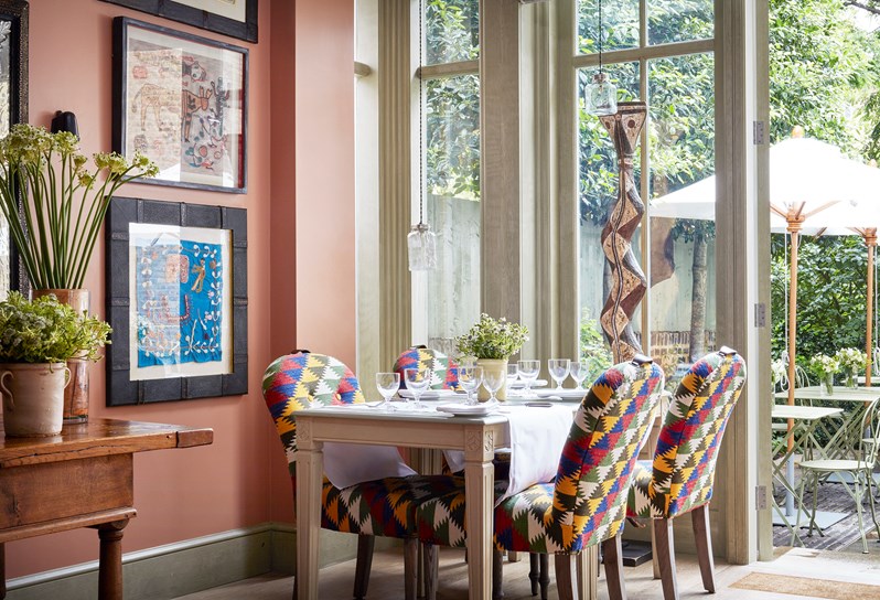 A corner image of the orangery showing a table set for dining next to a large window overlooking the garden at Number Sixteen.