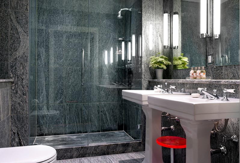 A grey granite bathroom with two basins, spacious shower and colourful stool.