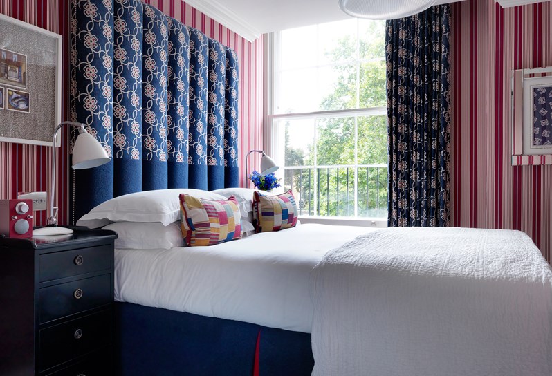 Superior room with a bold red stripped wallpaper containing spacious bed with bright blue patterned headboard and matching curtains.