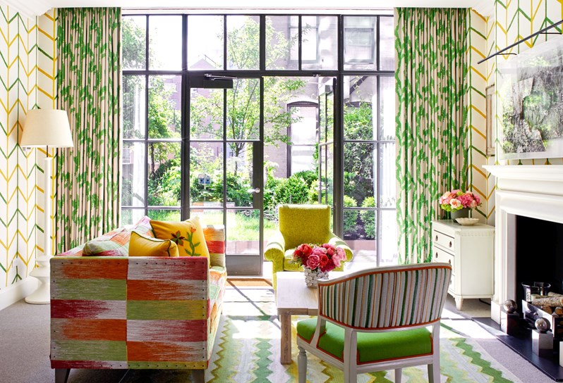 Shot of the living room of the Meadow Suite at the Crosby Street Hotel facing the large windows that are open to the garden. A sofa, a coffee table and two arm chairs in the centre of the room and a fire place on the right