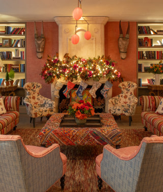 A wide shot of the drawing room at Warren Street Hotel. Two sofas and four arm chairs are placed around a coffee table. In the centre of the wall is a fireplace dressed with a festive garland and stockings