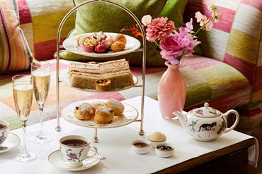 Afternoon tea displayed on a table in Refuel restaurant at The Soho Hotel. The fine bone china is Mythical Creatures by Kit Kemp for Wedgwood along side a 3 tier cake stand, sandwiches and scones.
