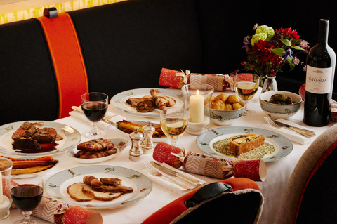 An image of the main dishes from the Christmas Day menu at Ham Yard Restaurant, Ham Yard Hotel. On the table, you can see  all on Sailor Fairwell crockery. Also on the table you can see Roast Bronze turkey with all the trimmings, Beef Wellington, ceps and truffle duxelles, red wine sauce and the Salmon coulibiac, Exmoor caviar butter sauce. Also on the table there are side dishes of of roast vegetables,  glasses of wine and champagne and festive flowers.   